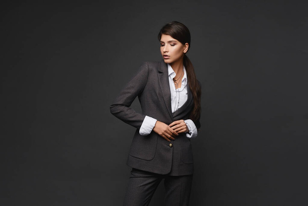 Fashion portrait of a young business lady in modish suit over grey background - Foto, Imagem