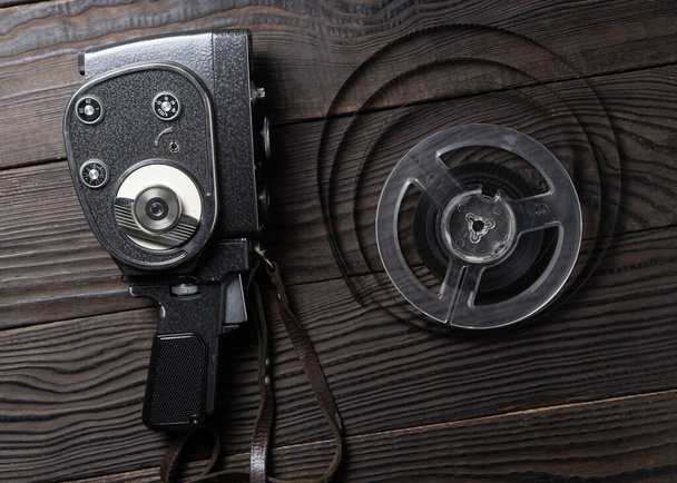 Old amateur movie camera and reel of film stock on dark wooden background - Fotoğraf, Görsel