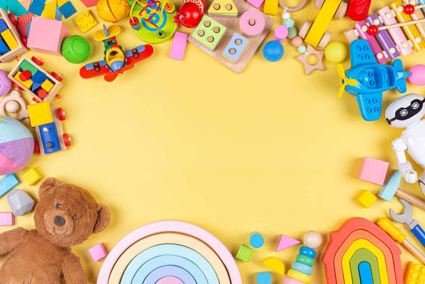 Bébé enfant fond de jouet. Jouets éducatifs en plastique et pelucheux en bois pour enfants sur fond jaune pastel. Vue de dessus, plan plat - Photo, image