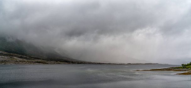 Μια πανοραμική θέα του τοπίου ενός φιόρδ με μυστικιστική ομίχλη και νεφοκάλυψη που κατεβαίνει από τα βουνά πάνω από τον ωκεανό - Φωτογραφία, εικόνα