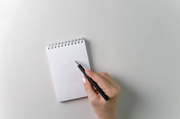 La mano di una donna tiene una penna nera su un quaderno bianco pulito. Copia spazio, layout - Foto, immagini