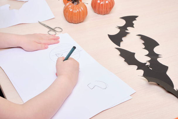 Halloween handmade decor.child makes halloween decor from paper, girl draws pumpkins and and ghosts on white paper - Foto, afbeelding