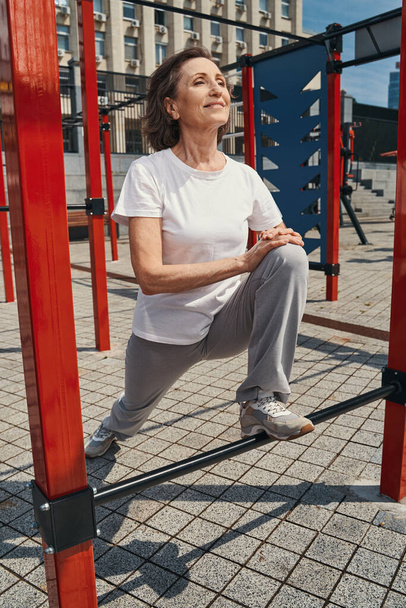 Happy elderly woman training body in city centre - Foto, Imagen