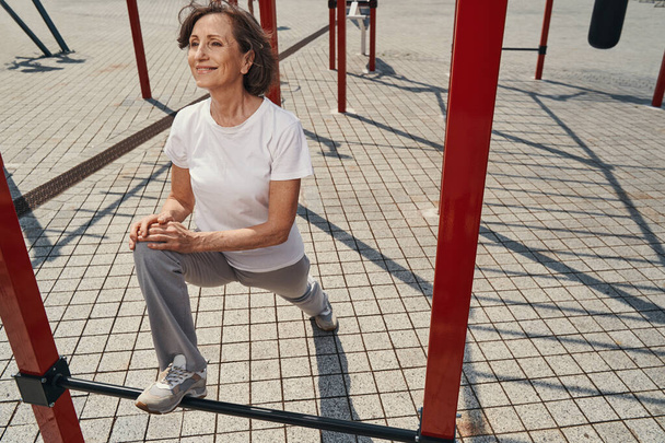 Merry mature female exercising with horizontal bars - Foto, Imagen