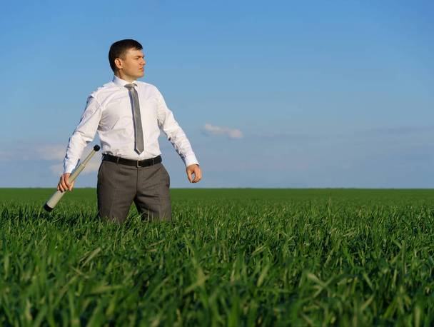 zakenman poseert met een verrekijker, hij kijkt in de verte en zoekt iets, groen gras en blauwe lucht als achtergrond - Foto, afbeelding