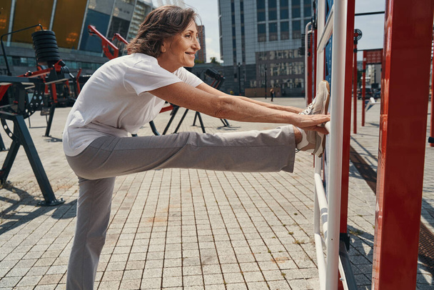 Smiling mature woman training flexibility in open air - Foto, imagen