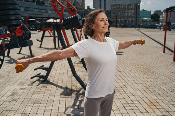 Gelukkig volwassen vrouw genieten van training met gewichten buiten - Foto, afbeelding