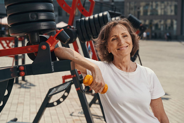Smiling athletic aged woman exercising in open air - Foto, Imagen
