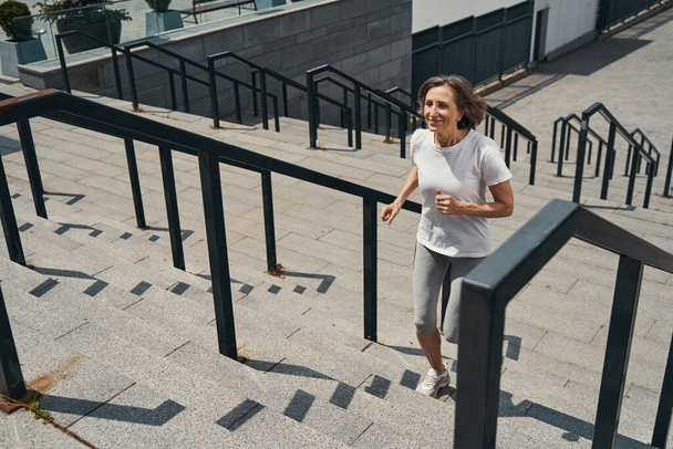 Χαμογελώντας ηλικιωμένη λεπτή γυναίκα πηγαίνει για τρέξιμο σε εξωτερικούς χώρους - Φωτογραφία, εικόνα