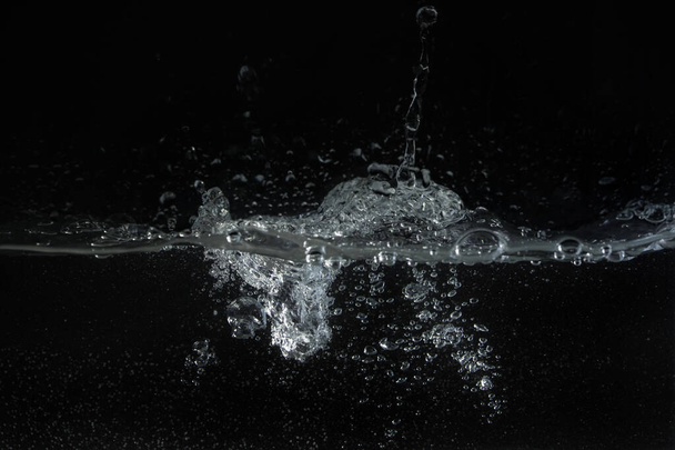 Water splashing as it's poured into aquarium tank, black background - 写真・画像