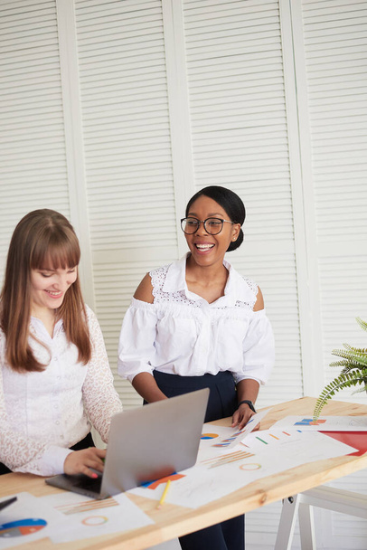 Lächelnde Frauen arbeiten in einem modernen Büro zusammen. Feminismus. Professionelle lächelnde Geschäftsfrauen stehen im Büro und diskutieren Geschäftspapiere - Foto, Bild