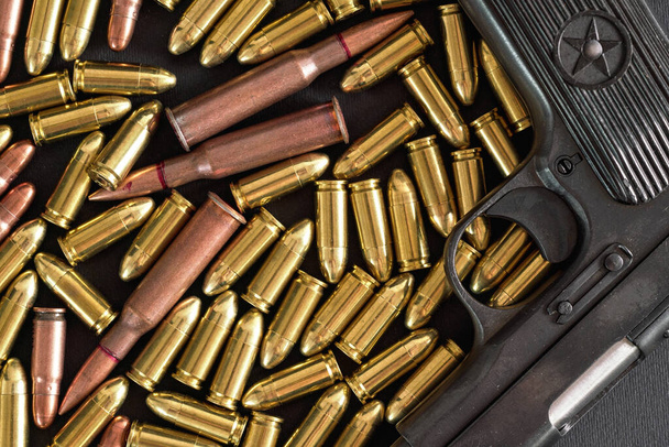 Yellow brass and brown bronze bullets, with black gun near, closeup detail from above - Foto, immagini