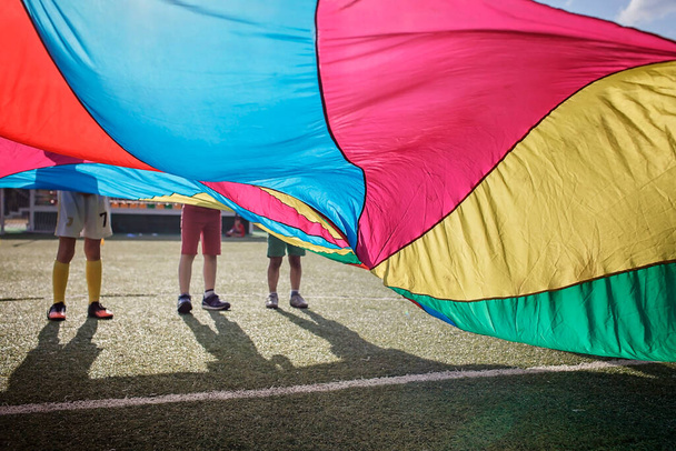 Group of friends playing and waving bright colorful parachute, outdoors party, summer school camp - Photo, Image
