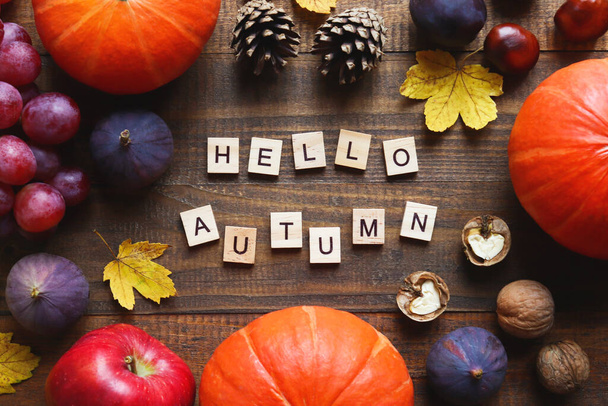 Autumn postcard with seasonal products and inscription Hello Autumn made from wooden letters. Pumpkins, grapes, figs, apples, pine cones, walnuts, and maple leaves. Top view, flat lay - Foto, Bild
