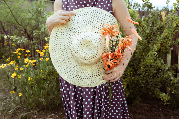 straw hatand a bouquet of tiger lily Lilium lancifolium in hands of woman. Summer and travel concept. - 写真・画像