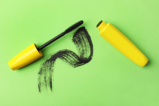Mascara for eyelashes and smear on green background, flat lay. Makeup product - Zdjęcie, obraz