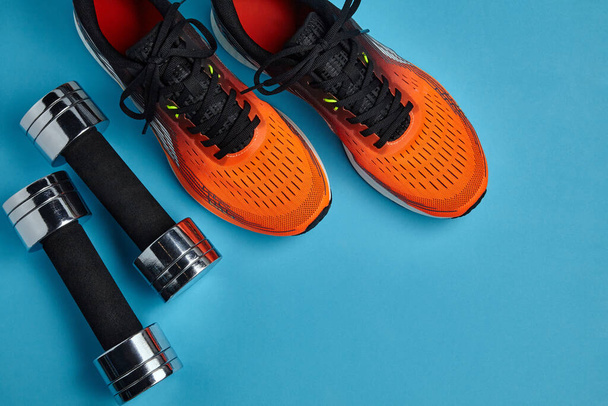 Orange sneakers and metal dumbbells on a blue background. Physical activity for health - Photo, image