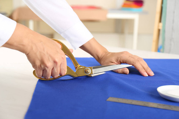 Seamstress cutting fabric at table in workshop, closeup - Фото, изображение