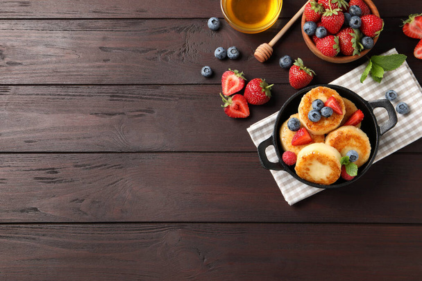 Delicious cottage cheese pancakes with fresh berries and honey on wooden table, flat lay. Space for text - Foto, Imagen