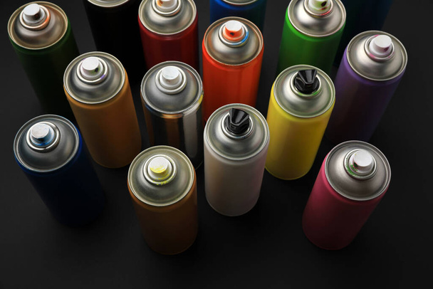 Cans of different graffiti spray paints on black background, above view - 写真・画像