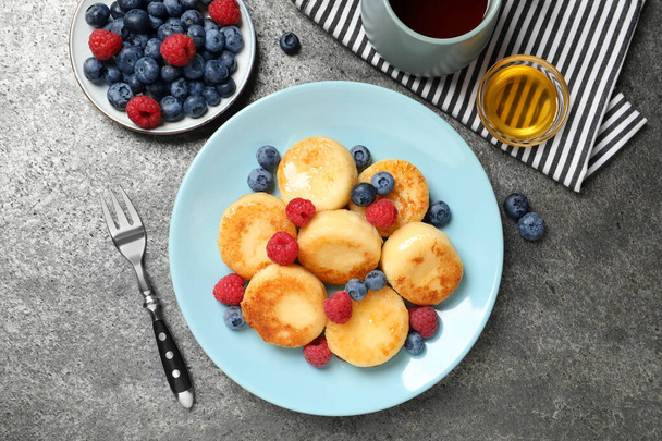 Delicious cottage cheese pancakes with fresh berries and honey on grey table, flat lay - Foto, Imagen