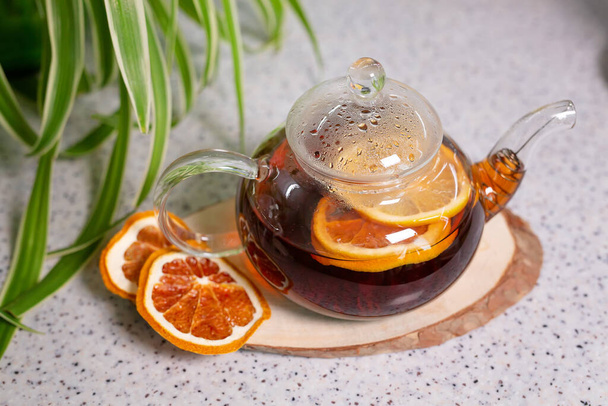 Kuuma teejuoma sitruunalla ja appelsiinilla, teekannu ja valkoinen kuppi, tarjoillaan herkullisen sitruunan ja kanelin kera. Tuoksuva ja lämmin tee. Laadukas kuva - Valokuva, kuva