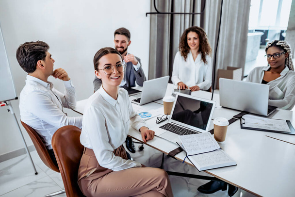 Young business people work in a spacious beautiful office together. Communication and break during work. The girl in the foreground is looking at the camera and smiling. - Photo, Image