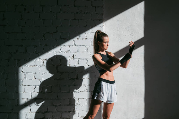 Női kickboxer áll egy boksz stúdióban, míg a por részecskék repül napkitörés fény háttér. - Fotó, kép