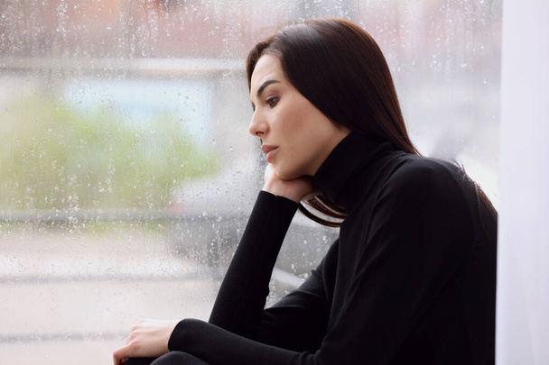 Depressed woman near window on rainy day, space for text - Фото, изображение
