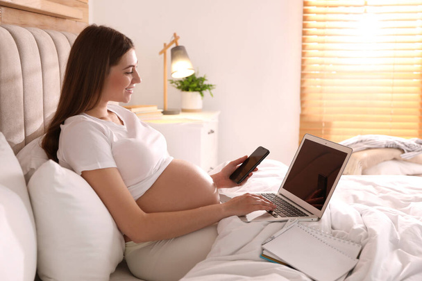 Pregnant woman working on bed at home. Maternity leave - Foto, imagen