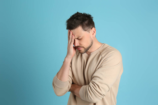 Man suffering from terrible migraine on light blue background - Fotoğraf, Görsel