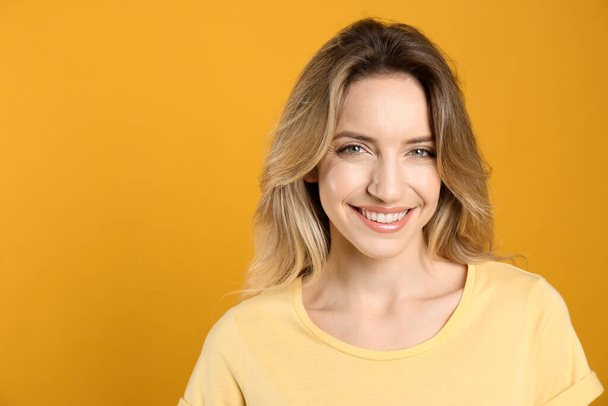 Portrait of happy young woman with beautiful blonde hair and charming smile on yellow background. Space for text - Фото, зображення