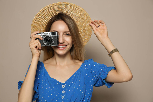 Beautiful young woman with straw hat and camera on beige background. Stylish headdress - Zdjęcie, obraz
