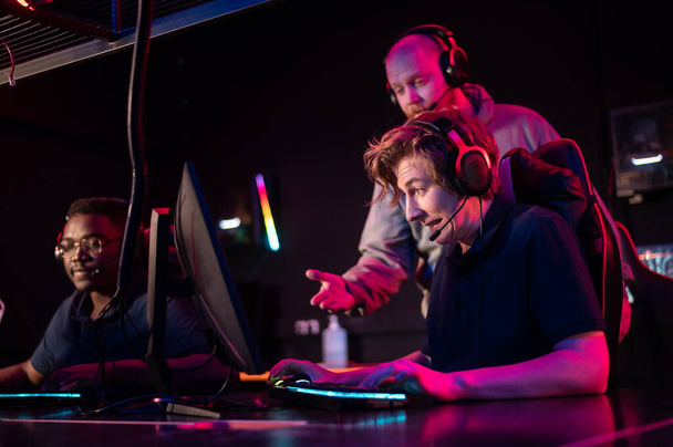 Durante o torneio Dota 2, dois caras da equipe jogam nos computadores, o treinador observa por trás - Foto, Imagem