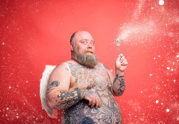 Gordo homem pensativo com barba, tatuagens e asas age como uma fada mágica - Foto, Imagem