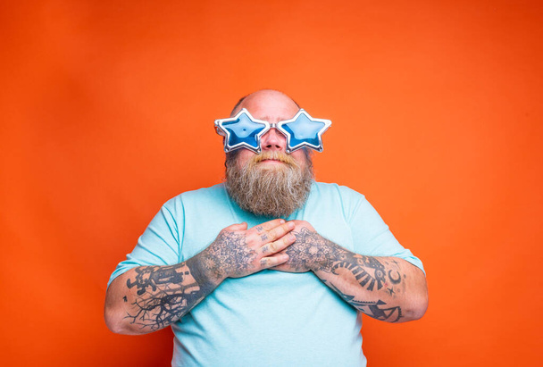 Dikke man met baard, tatoeages en zonnebril verrast voor iets - Foto, afbeelding