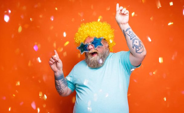 Hombre gordo con barba, tatuajes y gafas de sol baila música en una discoteca - Foto, imagen