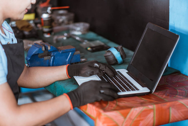 a bicycle mechanic wearing gloves uses a laptop computer while browsing - 写真・画像