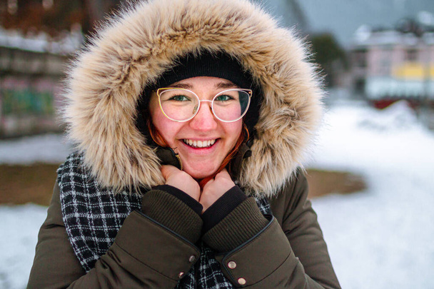 Щаслива молода жінка посміхається і захищає руку від холоду під пухнастою курткою взимку, як вона забула носити рукавички
 - Фото, зображення