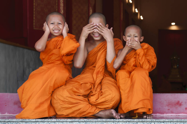 three Thai buddhist novice monk smiling and sitting together at temple gate - Φωτογραφία, εικόνα