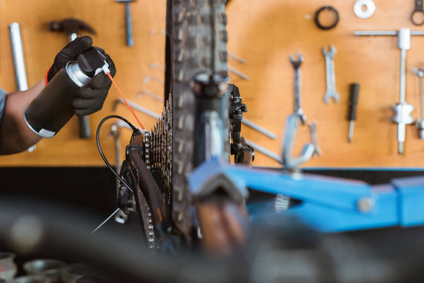 close up of a mechanics hand wearing gloves using chain lube lubricating the chain and freewheel - Fotó, kép