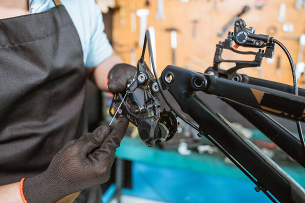 a mechanics hand in gloves pulls a cable while adjusting the rear derailleur - Foto, immagini