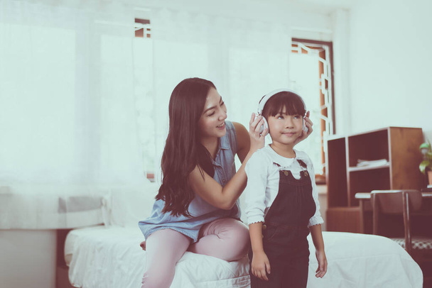 Asian single mom putting headphone to daughter at home,Happy and funny,Relaxing time - Foto, Imagen