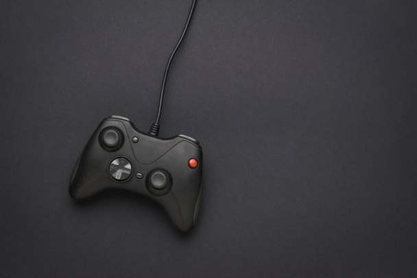 Una console di gioco nera con un filo su sfondo nero. Un dispositivo per giocare ai videogiochi. Posa piatta. - Foto, immagini