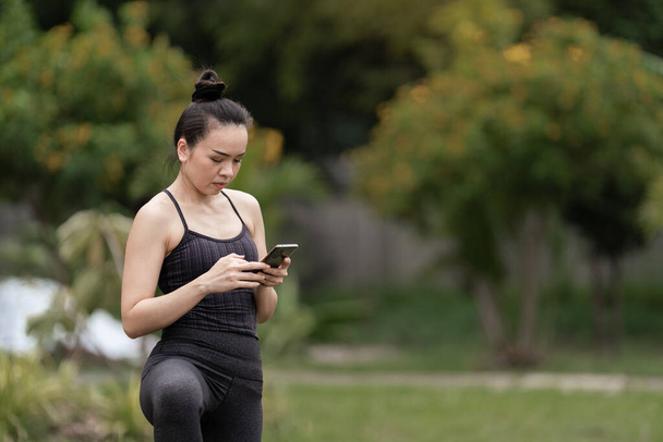 A confident middle-aged Asian woman in sports outfit doing yoga exercise on the yoga mat outdoor in the backyard in the morning. Young woman doing yoga exercise outdoor in nature public park - Foto, imagen