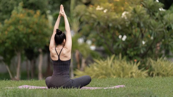 Уверенная азиатская женщина средних лет в спортивной одежде, делающая упражнения для йоги на коврике для йоги на открытом воздухе во дворе по утрам. Молодая женщина, занимающаяся йогой на открытом воздухе в природном парке - Фото, изображение