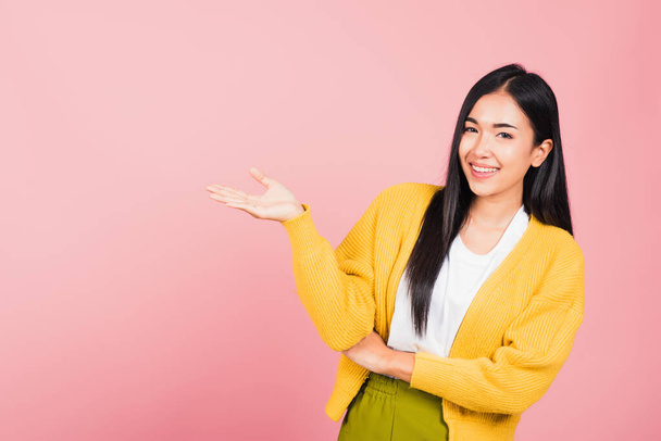 Asian happy portrait beautiful cute young woman smile standing presenting product holding something on palm away side, studio shot isolated on pink background with copy space, female show hand gesture - Foto, imagen