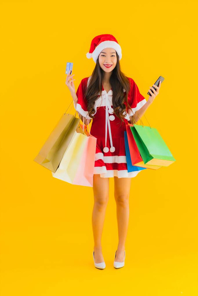 Portrét krásná mladá asijská žena nosit vánoční oblečení klobouk se spoustou nákupní tašky na žlutém izolovaném pozadí - Fotografie, Obrázek