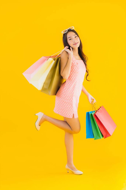 Πορτρέτο όμορφη νεαρή ασιατική γυναίκα με πολύχρωμο τσάντα ψώνια από πολυκατάστημα και εμπορικό κέντρο σε κίτρινο απομονωμένο φόντο - Φωτογραφία, εικόνα