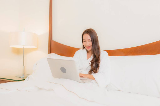 Güzel bir Asyalı kadın yatak odasının içinde dizüstü bilgisayar kullanıyor. - Fotoğraf, Görsel